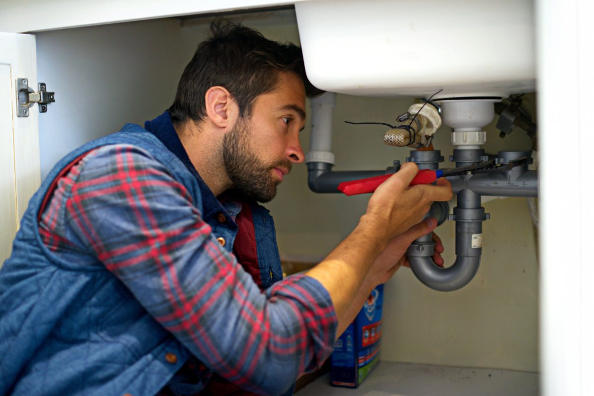 Man inspecting plumbing under a sink, focused and careful.