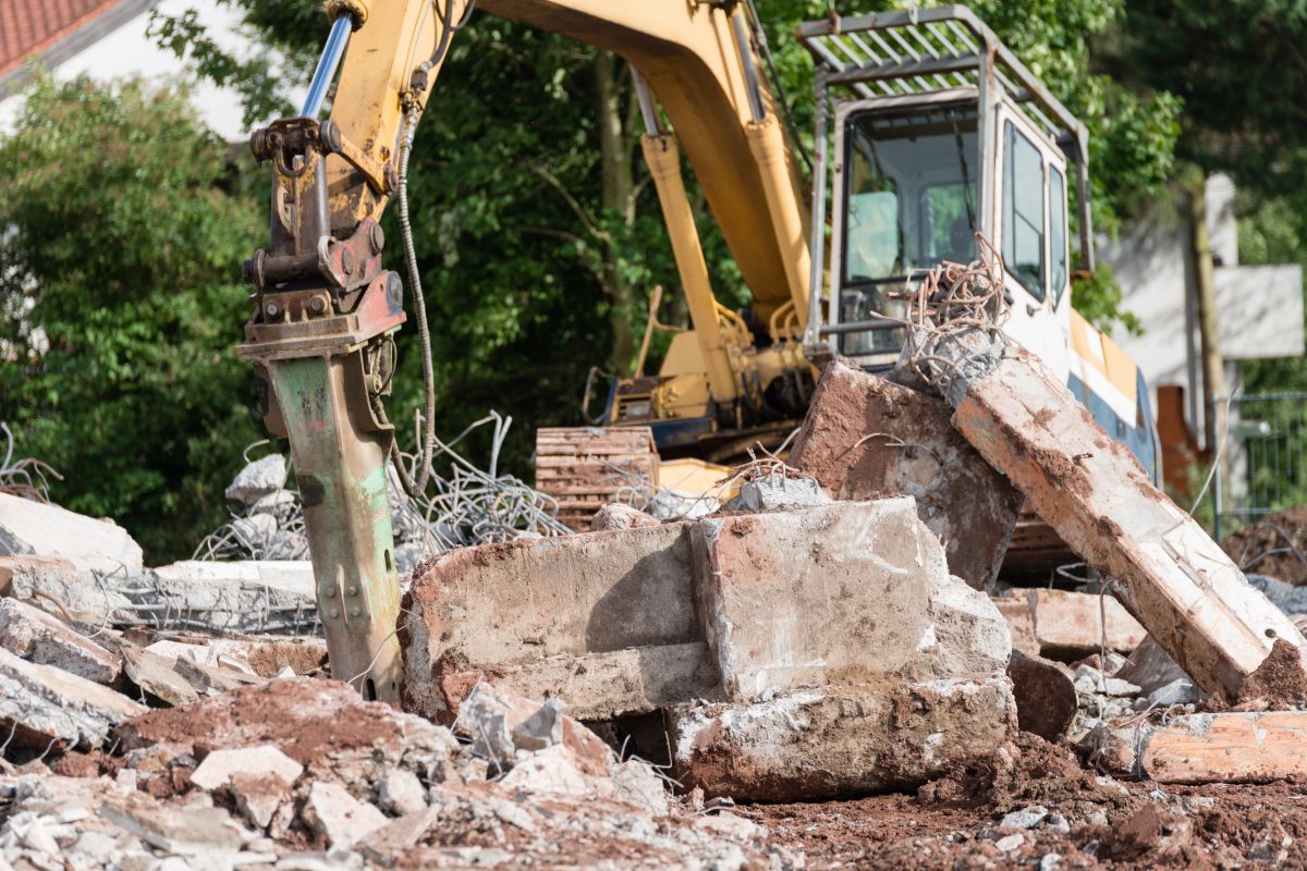 Excavator breaking concrete debris at a construction site.